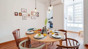 A dining area with a round table, wooden chairs, and a variety of breakfast items. There are framed pictures on the wall and a window providing natural light. - Sweett | Rocafort 104 (Barcelona)