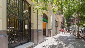 A street view with a building featuring ornate metal gates, a visible entrance, and a sidewalk with pedestrians. - Sweett | Rocafort 104 (Barcelona)