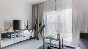 Una sala de estar moderna con un televisor de pantalla plana sobre un mueble de vidrio, una mesa de centro con un libro y un sofá.