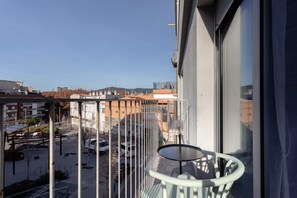 Een balkon met een tafel en stoelen, met uitzicht op een parkeerplaats en gebouwen.