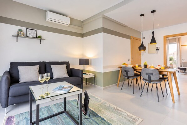 A modern living room with a sofa, coffee table, and dining area with chairs and a table.