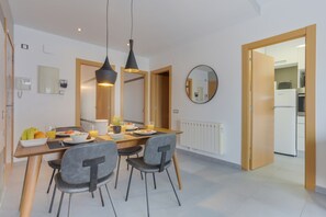 Een moderne eetruimte met een houten tafel, grijs gestoffeerde stoelen, hanglampen en uitzicht op de keuken.