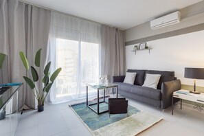 Un salon moderne avec un canapé, une table basse, une lampe et une grande fenêtre ornée de rideaux légers.