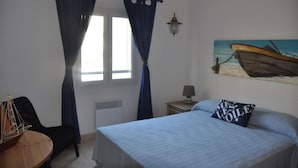 A bedroom with a bed, a chair, a table, a lamp, and a painting of a boat. - Pavilion with terrace sea view and pool in residence (SAINT PIERRE LA MER)
