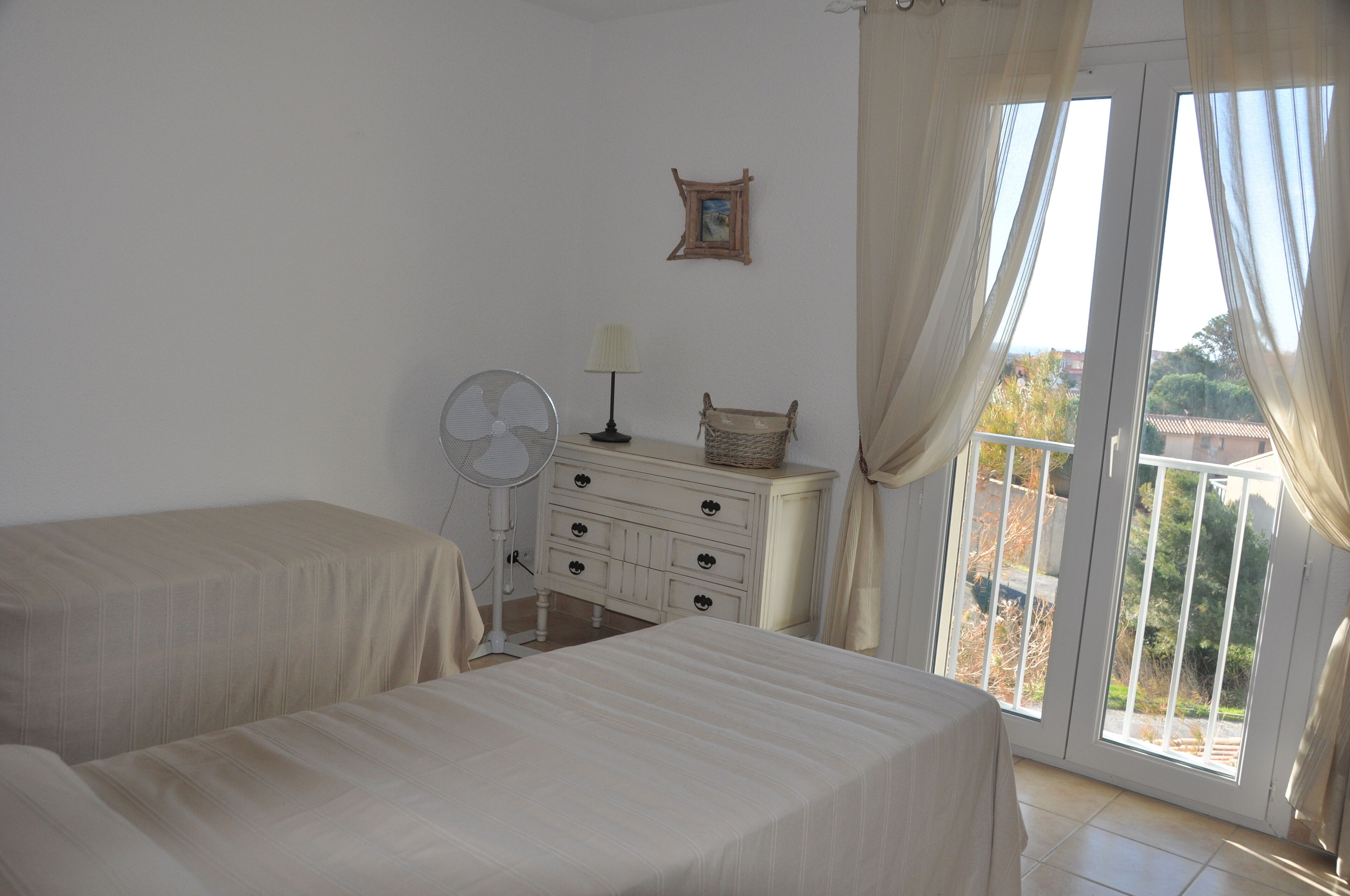 A bedroom with two beds, a dresser, a fan, and a window with curtains.