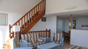 A living room with a wooden staircase, striped sofas, and a dining area. - Pavilion with terrace sea view and pool in residence (SAINT PIERRE LA MER)