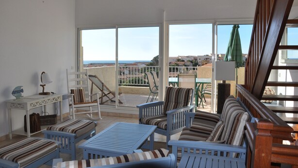 A balcony with a view of the sea, furnished with blue chairs and a striped sofa, and a table with a lamp. - Pavilion with terrace sea view and pool in residence (SAINT PIERRE LA MER)