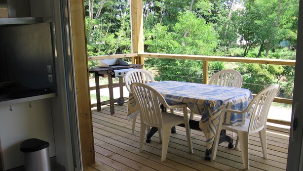 A covered outdoor patio with a table and chairs, a grill, and a trash can. - MATHES la PALMYRE house WOOD (BBC label) (Les Mathes)