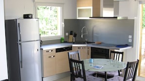 A compact kitchen with a refrigerator, dishwasher, and a dining table with chairs. - MATHES la PALMYRE house WOOD (BBC label) (Les Mathes)