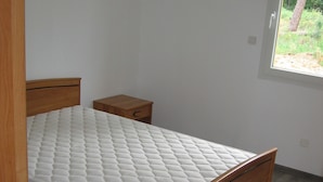 A bedroom with a wooden bed, a nightstand, and a window with a view of greenery. - MATHES la PALMYRE house WOOD (BBC label) (Les Mathes)
