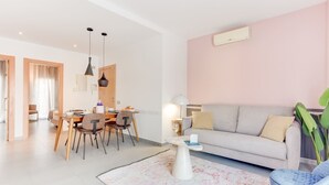 Un salon moderne avec un canapé, un coin repas comprenant des chaises et une table, et une grande plante.