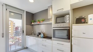 Une cuisine moderne avec des armoires blanches, un four à micro-ondes, un four et un réfrigérateur. Une fenêtre offre une vue sur les bâtiments environnants.