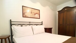 A neatly made bed with white linens, a wooden nightstand, a wooden wardrobe, and a framed picture on the wall. - Appartamento Acton - Piano Terra (Ugento)