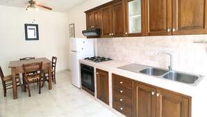 A kitchen with wooden cabinets, a white refrigerator, a stove, and a sink. - Appartamento Acton - Piano Terra (Ugento)