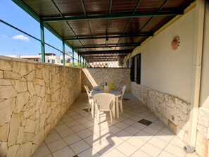 A covered patio with a stone wall, a tiled floor, and a table with chairs. - Appartamento Acton - Piano Terra (Ugento)