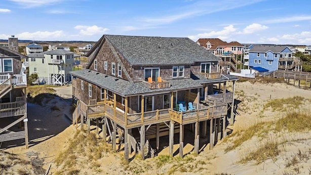 A beachfront house with a deck, multiple windows, and a sandy beach in the background. - Salt Therapy OBX | Oceanfront | Dog Friendly, Hot Tub | Nags Head (Nags Head)