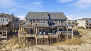 A beachfront house with a deck, multiple windows, and a sloped roof. - Salt Therapy OBX | Oceanfront | Dog Friendly, Hot Tub | Nags Head (Nags Head)