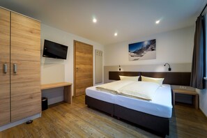 A modern bedroom with a large bed, wooden wardrobe, a flat-screen TV, and a painting on the wall. - Fernerblick Apartments (Tux)