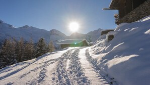 Un sentier de montagne enneigé menant à un bâtiment en bois doté de fondations en pierre.