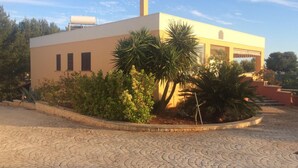 A modern building with a flat roof, a water tank on the roof, and a paved courtyard with a palm tree and shrubs. - Appartamento Apollo (Morciano di Leuca)