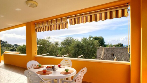 A balcony with a table and chairs, a view of trees and a distant building. - Appartamento Apollo (Morciano di Leuca)