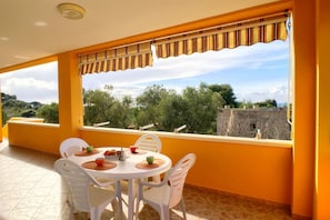 A balcony with a table and chairs, a view of trees and a distant building.