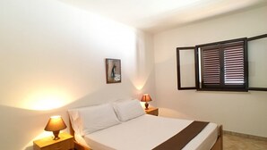 A single bed with a wooden frame, white bedding, and a brown throw blanket. There are two bedside tables with lamps, one on each side of the bed. A framed picture hangs on the wall above the bed. - Appartamento Apollo (Morciano di Leuca)