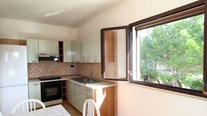 Une cuisine compacte avec un coin repas, une fenêtre donnant sur les arbres et un pare-feu en carreaux.
