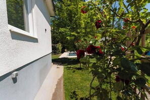 A residential backyard with a swimming pool, a white house wall, and a garden with roses. - Adventure Cottage by the Sava River (Bled)