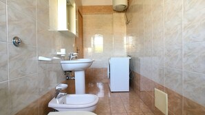A bathroom with a toilet, bidet, sink, and a small washing machine. - Appartamento Emma (Gallipoli)