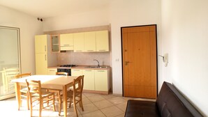 A compact kitchen with a dining table and chairs, a sofa, and a wooden door. - Appartamento Emma (Gallipoli)