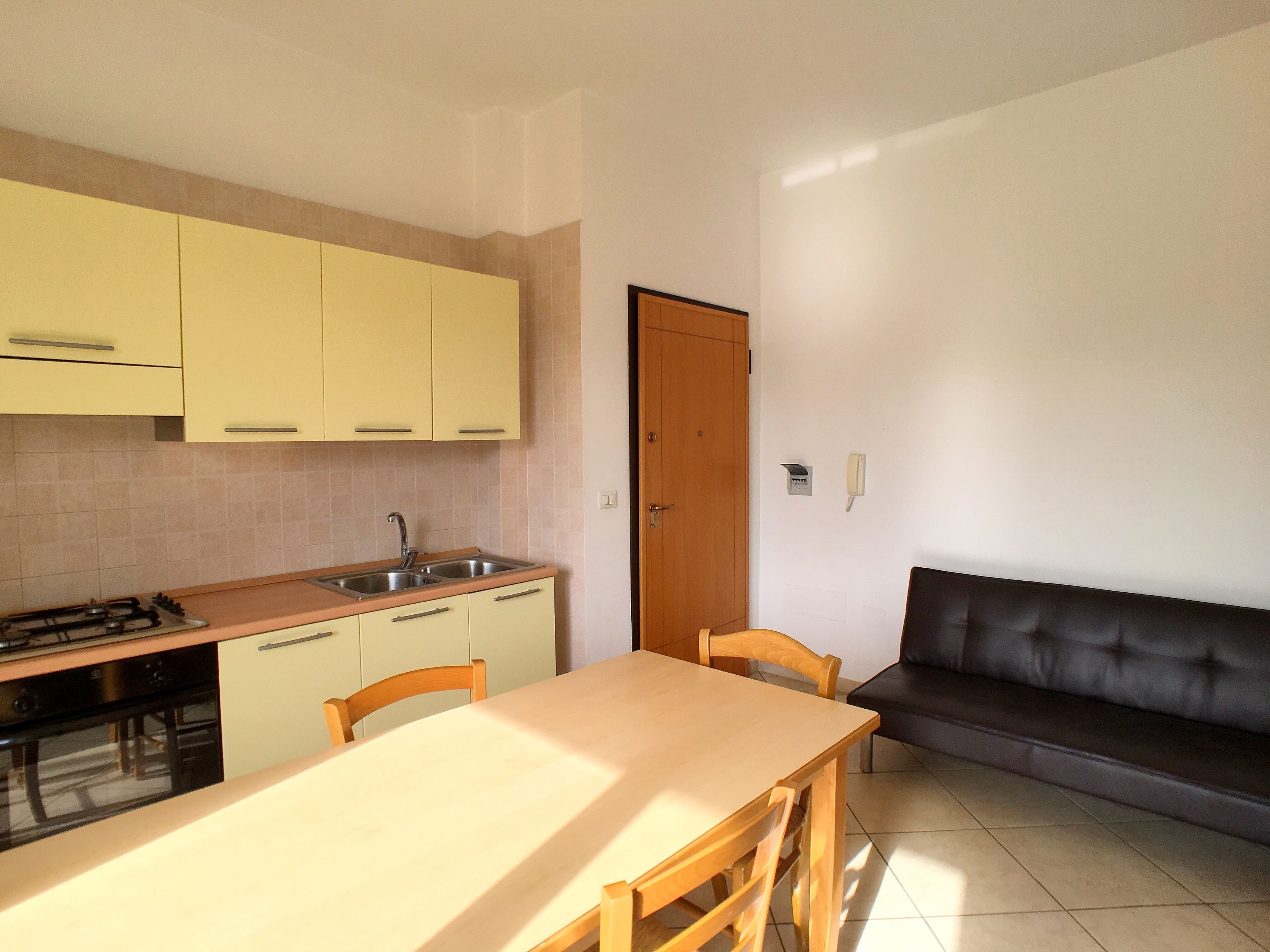 A compact kitchen with a dining table and chairs, a sofa, and a door.