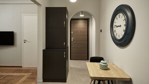 Un couloir avec une porte en bois, une commode sombre, une horloge murale ronde et une petite table sur laquelle est posé un objet décoratif.