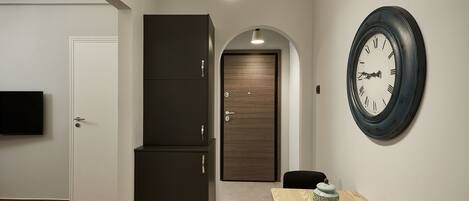 A hallway with a wooden door, a dark cabinet, a round wall clock, and a small table with a decorative item.