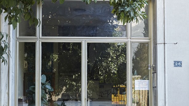 Une entrée d’immeuble avec une porte en verre, un numéro bien visible « 26 », et des marches menant à cette entrée.