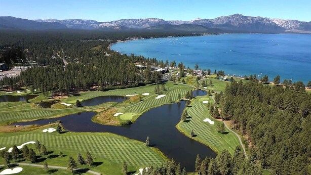 Een golfbaan met diverse waterhindernissen, omringd door dichte bossen en bergen op de achtergrond.