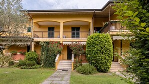 A two-story building with a yellow facade, a central entrance with steps, and a small garden with a stone pathway. - Casa @rena - Pool - Patio - Pet friendly - LAKE (Sirmione)