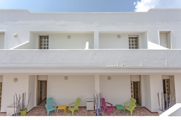 A white building with multiple windows and doors, a tiled floor, and colorful plastic chairs arranged outside. - Margherita - Piano Ribassato (Taviano)