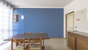 A dining area with a wooden table and chairs, a blue wall, and a kitchen counter. - Margherita - Piano Ribassato (Taviano)
