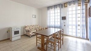 A room with a dining table, chairs, a sofa, a TV, and a window with curtains. - Margherita - Piano Ribassato (Taviano)