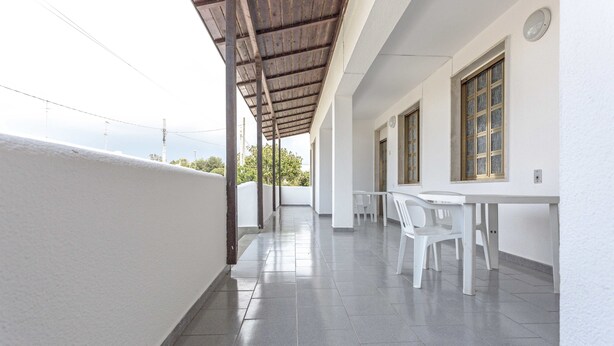 A covered outdoor area with a tiled floor, white walls, and a table with chairs.