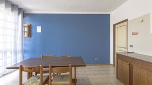 A dining area with a wooden table and chairs, a blue wall, and a kitchen counter.