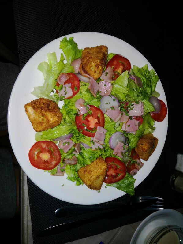 A plate of salad with lettuce, tomatoes, onions, and breaded chicken pieces.