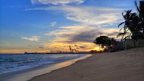 A beach with a clear sky, calm sea, and distant industrial structures.