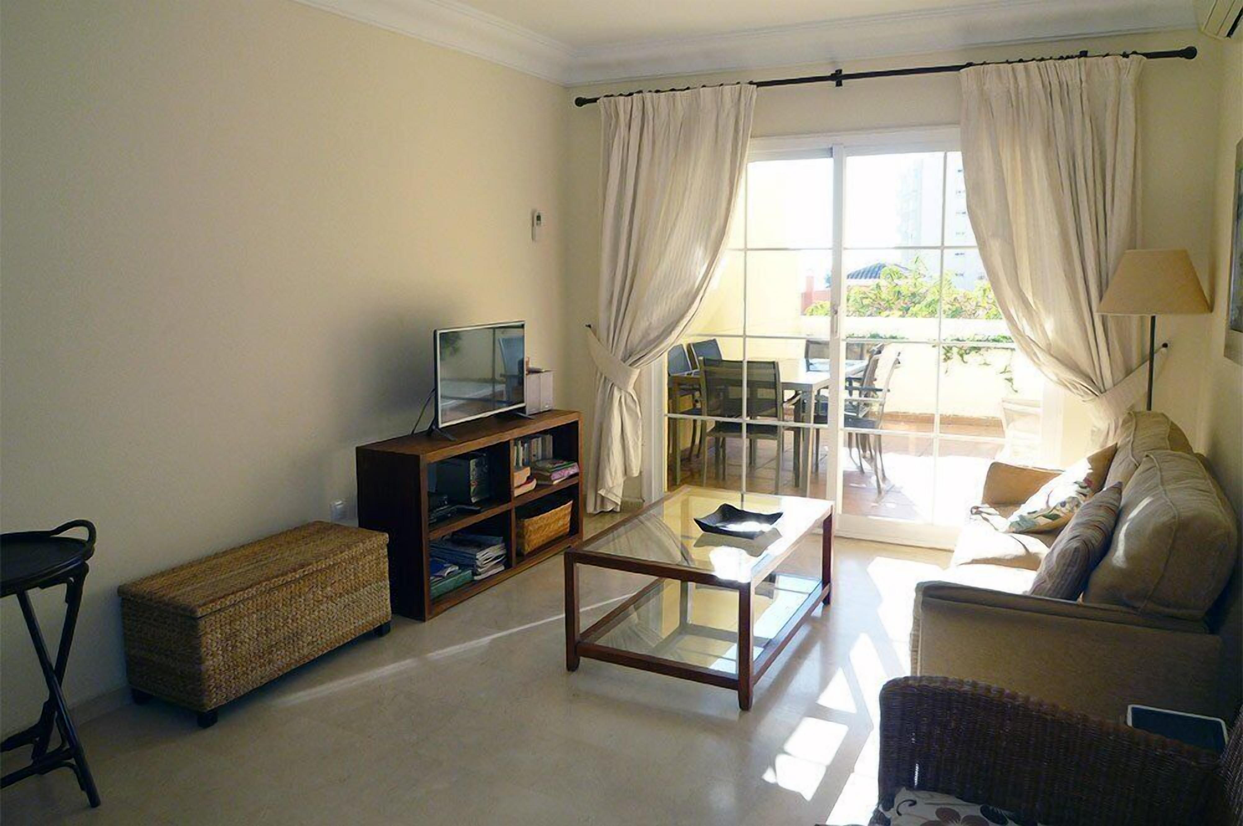 A living room with a sofa, a glass coffee table, a television on a wooden stand, and a bookshelf.