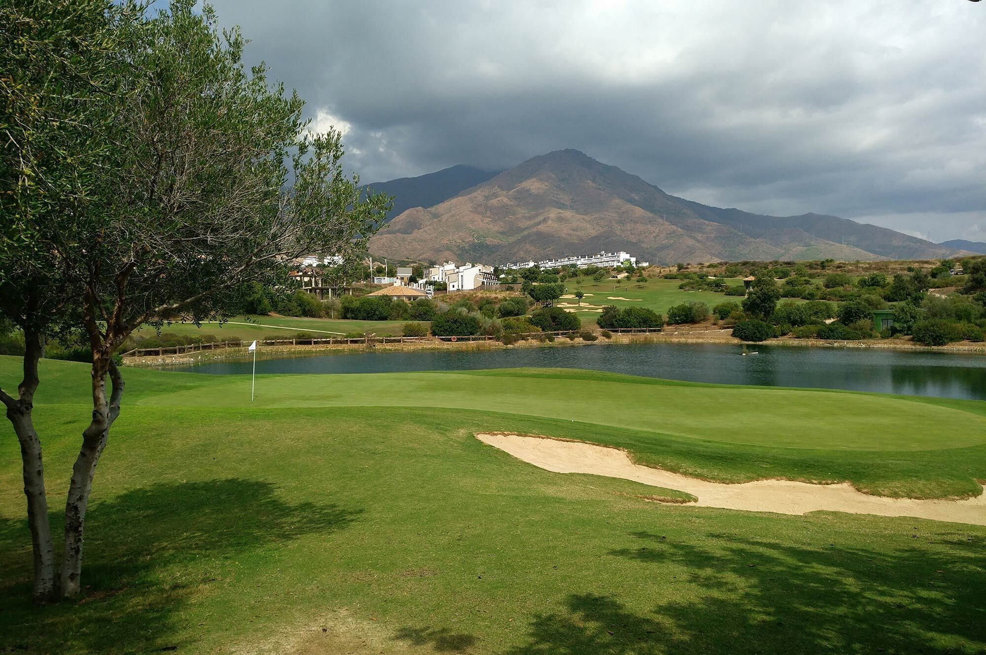 Un campo de golf con un lago, árboles y una montaña al fondo.