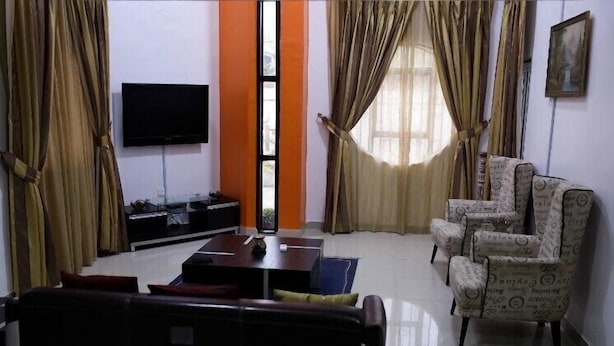 A living room with a sofa, armchairs, a coffee table, a TV, and curtains.