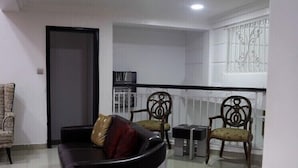 A modern living room with a black sofa, two wooden chairs, a small table, and a glass partition.