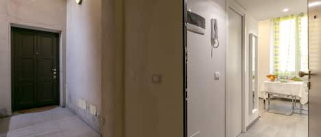 Ein Flur mit einer dunklen Tür, einer weißen Wand inklusive Lichtschalter und einem Essbereich mit Tisch und Stühlen.