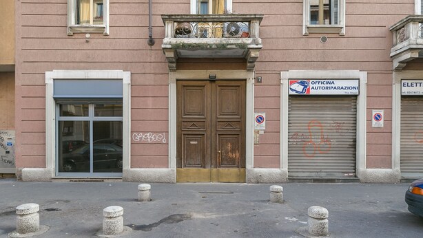 A building with a closed metal shutter door, a wooden double door, and a balcony with ornate metal railings. - notaMi - NotaMi Red Studio (Milan)